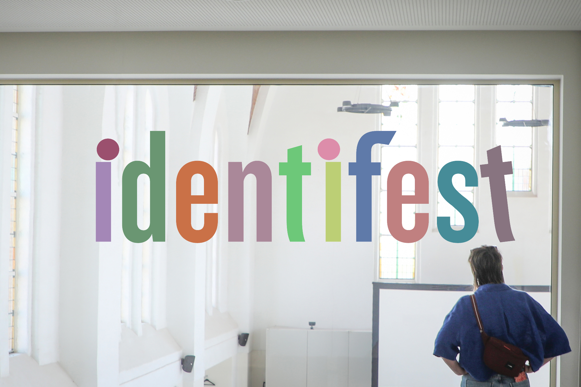 Kleurrijke IDENTIFEST-letters op een glazen wand in een lichte ruimte
