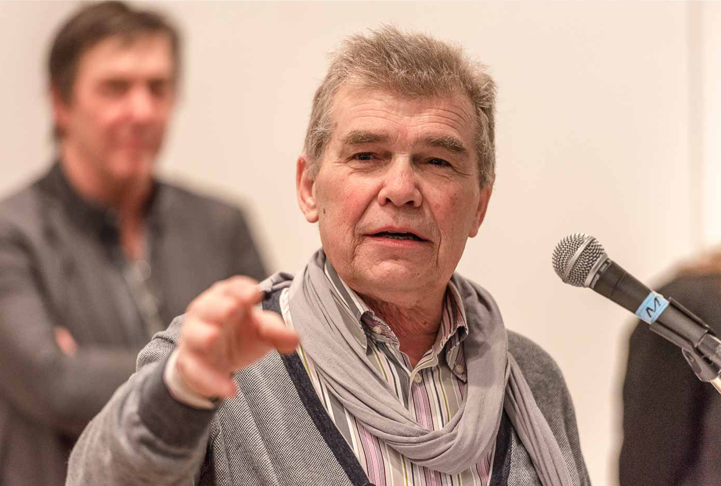 Spreker met sjaal aan de microfoon tijdens een opening