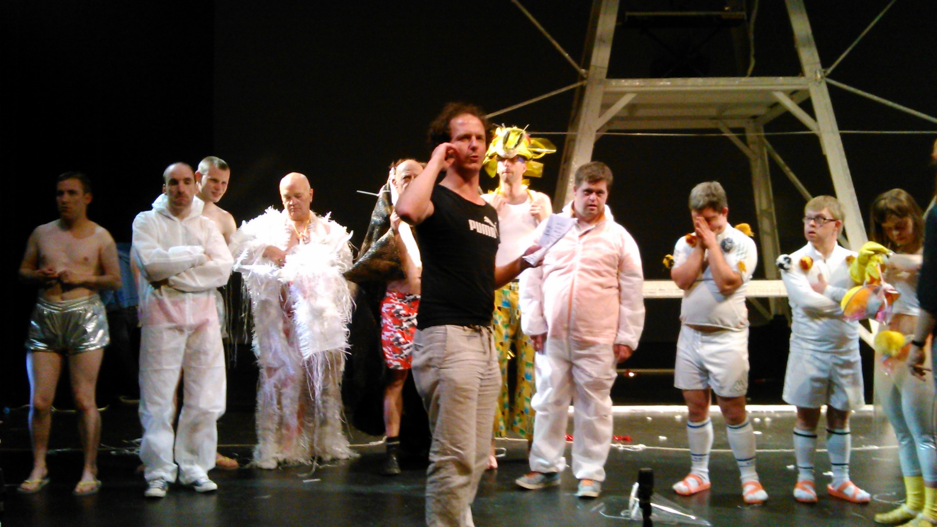 Ensemble van performers in witte pakken en kostuums op scène