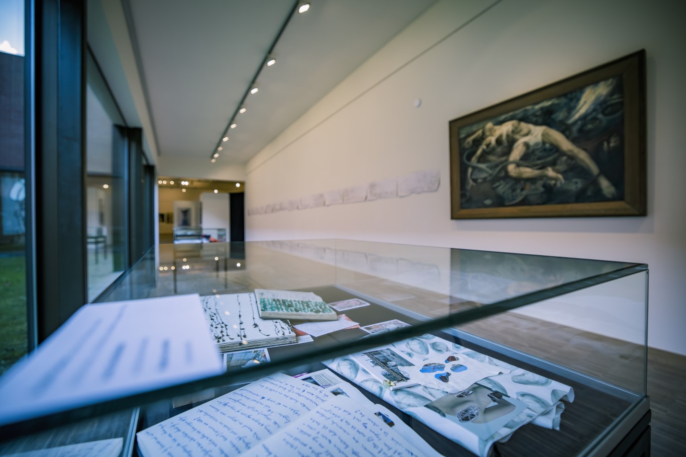 Vitrine met schetsboeken en schilderij op de achtergrond