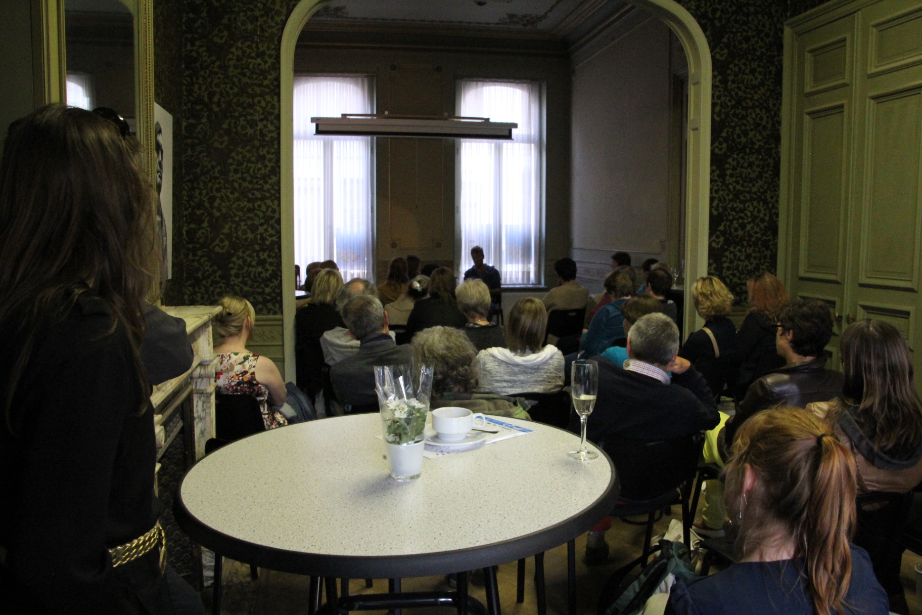 Publiek luistert in een zaal met groen behang