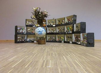 Installatie met houten kisten in halve cirkel rond een centrale sculptuur